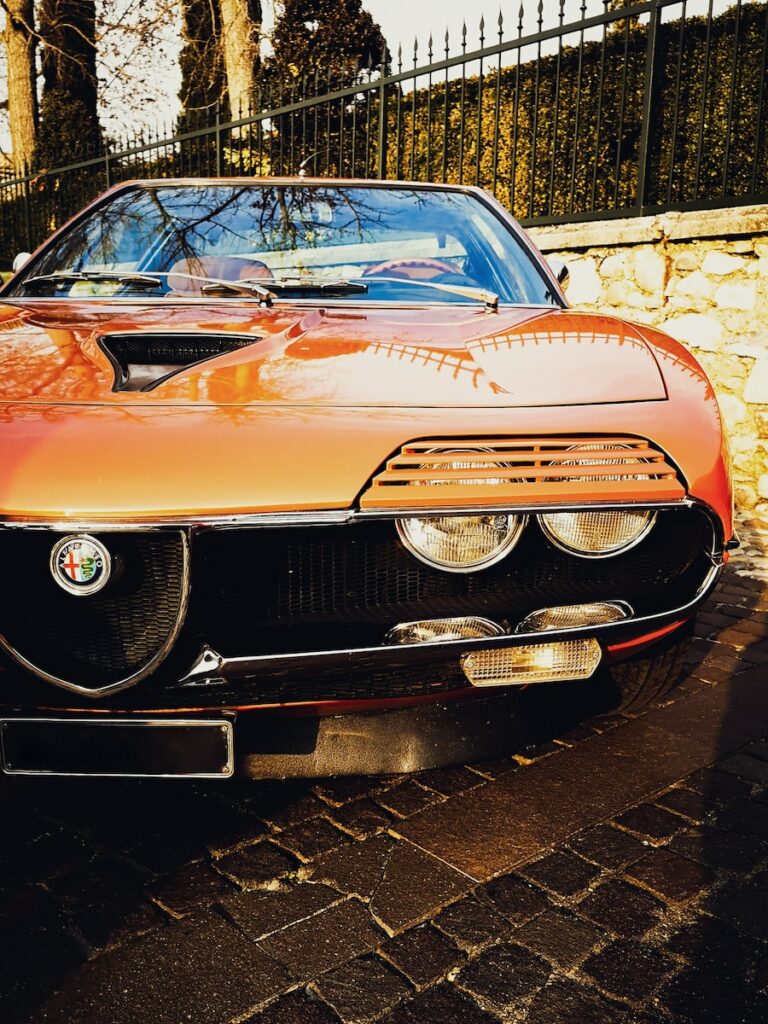 orange classic car parked beside brick wall